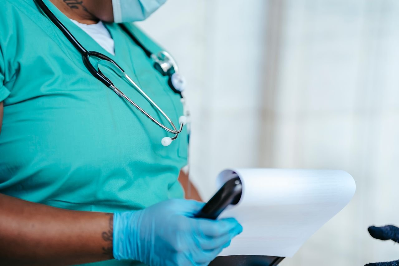 Side view of crop anonymous tattooed ethnic female medic in uniform with stethoscope and papers on clipboard